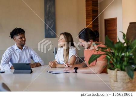 Diverse group discussing project at office table with tablet and notebook Diverse group discussing project at office table with tablet and notebook 135628601