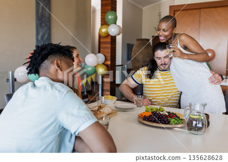 Friends enjoying meal together at home, sharing laughter and conversation Friends enjoying meal together at home, sharing laughter and conversation 135628628