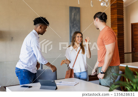 Friends greeting each other with smiles and handshakes in modern living room 135628631