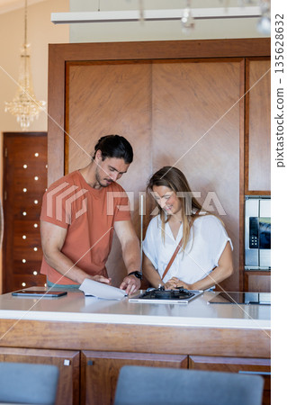 Couple reviewing documents together in modern kitchen, smiling and collaborating 135628632