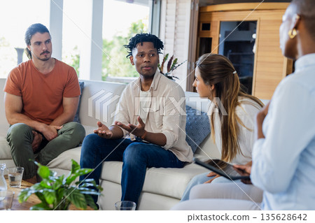 Discussing ideas, diverse friends sharing insights in thoughtful home conversation Discussing ideas, diverse friends sharing insights in thoughtful home conversation 135628642