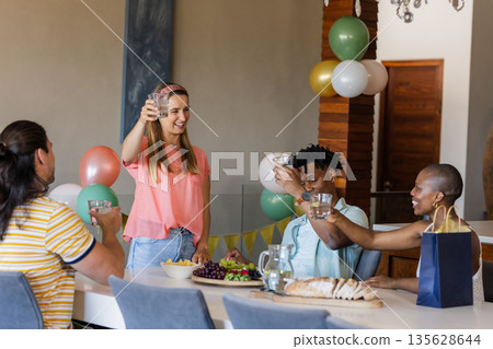 Friends celebrating at home, raising glasses and enjoying snacks together Friends celebrating at home, raising glasses and enjoying snacks together 135628644
