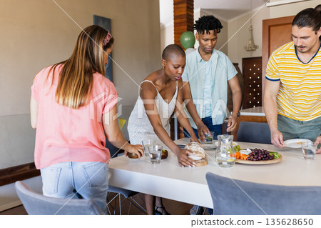 Friends preparing table with bread and fruit platter for casual gathering at home Friends preparing table with bread and fruit platter for casual gathering at home 135628650