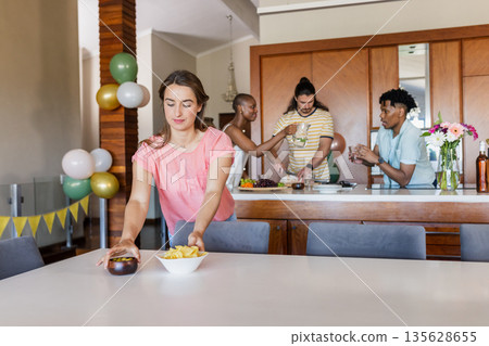 Friends preparing snacks and drinks in kitchen, enjoying casual gathering at home 135628655