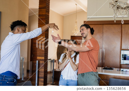 Friends celebrating new home, exchanging keys with excitement in modern kitchen Friends celebrating new home, exchanging keys with excitement in modern kitchen 135628656