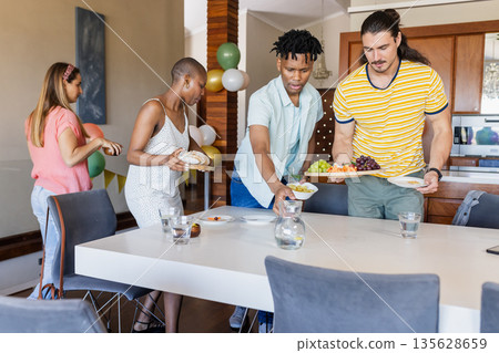 Friends setting table with food and drinks for casual gathering at home 135628659