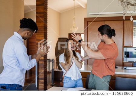 Friends celebrating success at home, clapping and smiling with excitement 135628660