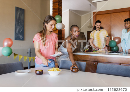 Friends preparing snacks and setting table for indoor gathering at home Friends preparing snacks and setting table for indoor gathering at home 135628670