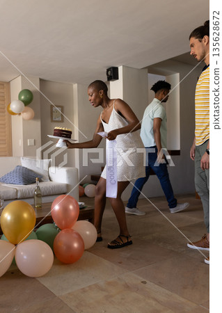 Woman in white dress placing cake on table at home during celebration 135628672
