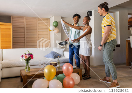 Celebrating graduation, diverse friends smiling and holding banner in living room Celebrating graduation, diverse friends smiling and holding banner in living room 135628681