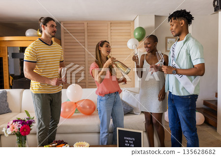 Friends celebrating new job with champagne and balloons in living room Friends celebrating new job with champagne and balloons in living room 135628682