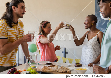 Friends toasting with glasses, enjoying casual gathering with snacks and drinks Friends toasting with glasses, enjoying casual gathering with snacks and drinks 135628696