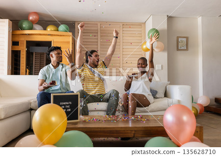 Friends celebrating new job with confetti and balloons in living room 135628710