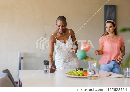 Friends enjoying casual gathering, setting table with snacks and drinks at home 135628714