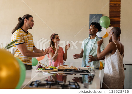Celebrating at home, friends sharing conversation and laughter around kitchen island 135628716