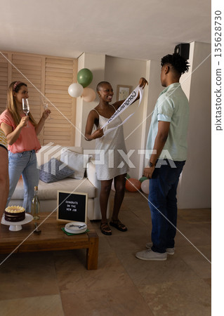 Friends celebrating new job with cake and champagne in cozy living room 135628730