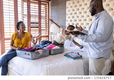 Family packing suitcase on bed, preparing for vacation with excitement and laughter 135628757
