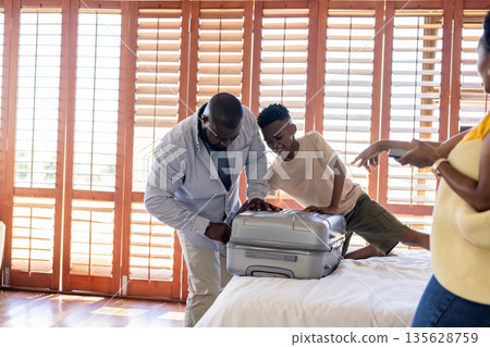 Father and son packing suitcase on bed, preparing for family vacation 135628759