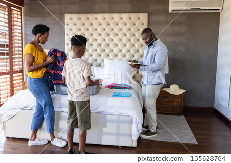 Family packing suitcase together in bedroom, preparing for vacation trip Family packing suitcase together in bedroom, preparing for vacation trip 135628764