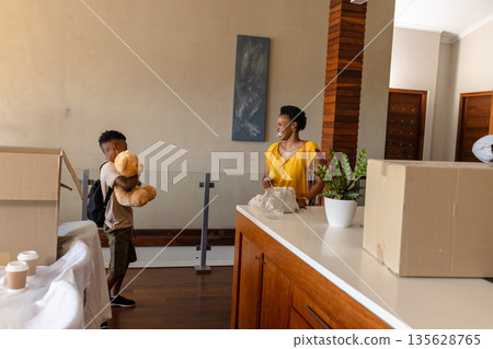Mother and son unpacking boxes at new home, smiling and holding teddy bear 135628765