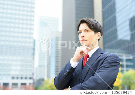 辦公區路邊綠樹成蔭，一位穿著西裝的男士正在等候。 135629434