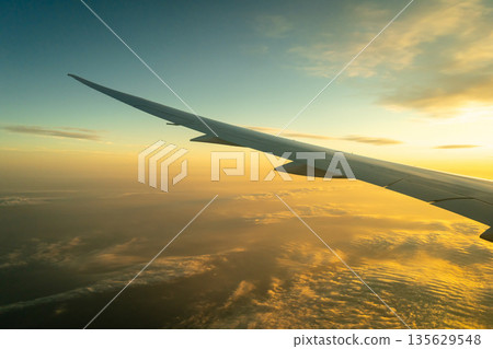 Airplane wing above the clouds during golden hour flight 135629548