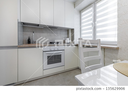 Modern studio kitchen with white cabinets, built-in appliances and dining table 135629906