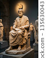 Ancient marble statue of philosopher seated in museum with other sculptures in background 135630043