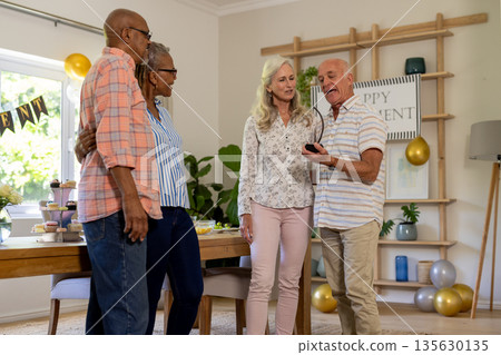 Celebrating birthday at home, senior friends smiling and sharing joyful moments together 135630135