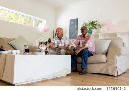 Senior friends enjoying coffee and cake together in cozy living room setting Senior friends enjoying coffee and cake together in cozy living room setting 135630142