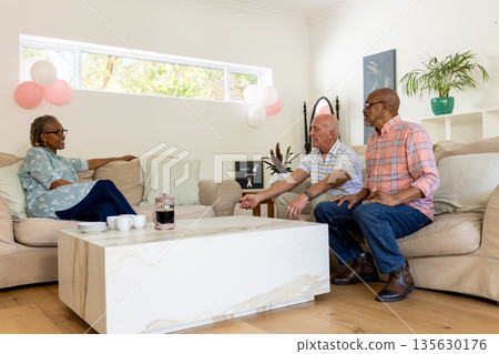 Senior friends enjoying coffee and conversation in cozy living room setting Senior friends enjoying coffee and conversation in cozy living room setting 135630176