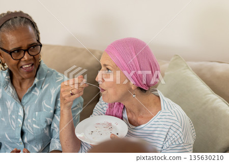 Senior women enjoying dessert together, sharing laughter and conversation on sofa Senior women enjoying dessert together, sharing laughter and conversation on sofa 135630210
