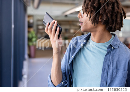 Using smartphone voice assistant, man multitasking efficiently in modern office 135630223