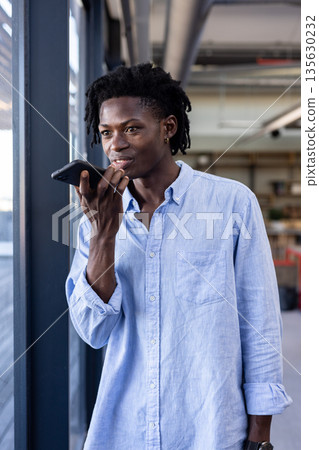 African American man in office speaking into smartphone, looking thoughtful African American man in office speaking into smartphone, looking thoughtful 135630232