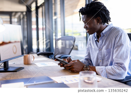 African American man using tablet and computer at office, analyzing data charts 135630242