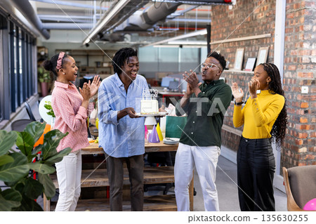 Celebrating birthday with cake, African American colleagues smiling joyfully in modern office 135630255