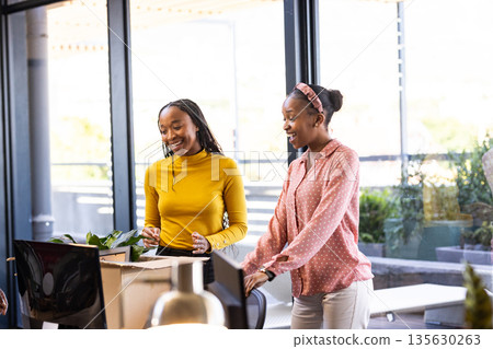 Two women collaborating in modern office, smiling and discussing creative project 135630263