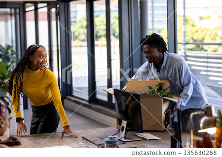 Unpacking box in modern office, African American colleagues smiling and collaborating 135630268