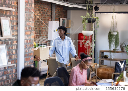 Young professional carrying box in modern office, colleagues working at desks Young professional carrying box in modern office, colleagues working at desks 135630276