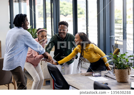 Diverse team celebrating success with group handshake in modern office 135630288