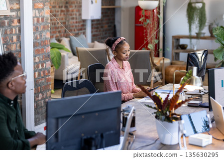 Colleagues collaborating at modern office desk, focusing on digital projects 135630295