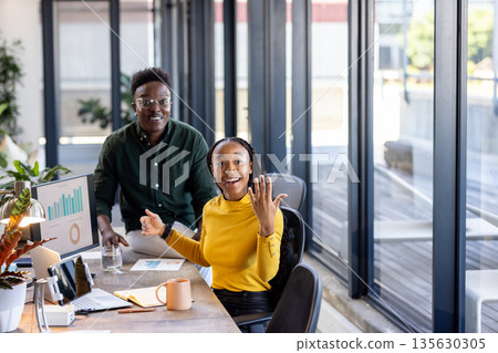 African American colleagues discussing project at office desk, smiling and engaged 135630305