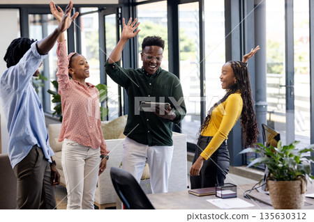 African American colleagues celebrating success with high fives in modern office African American colleagues celebrating success with high fives in modern office 135630312