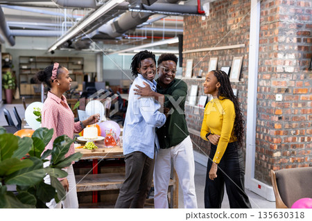Celebrating in office, African American colleagues sharing joyful hugs and laughter Celebrating in office, African American colleagues sharing joyful hugs and laughter 135630318