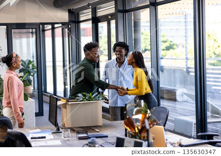Colleagues greeting each other with handshake in modern office, smiling warmly Colleagues greeting each other with handshake in modern office, smiling warmly 135630347