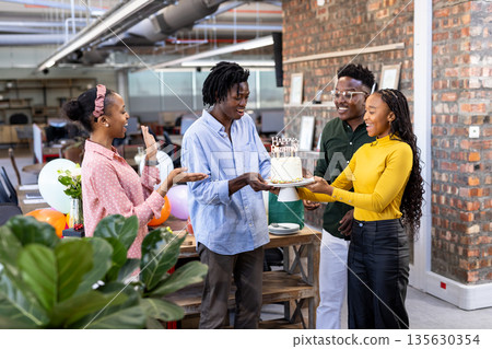 Presenting cake, African American colleagues celebrating birthday in modern office 135630354