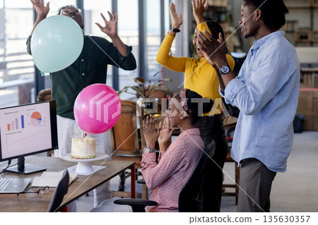 Celebrating in office, diverse team clapping around desk with cake and balloons 135630357