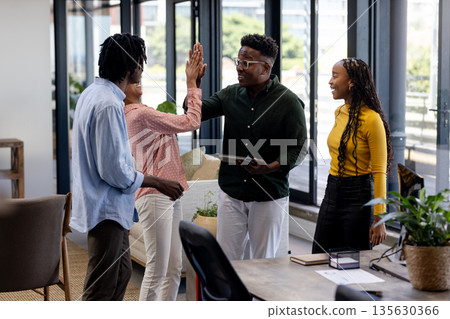 Celebrating successful teamwork, African American colleagues high-fiving in modern office 135630366