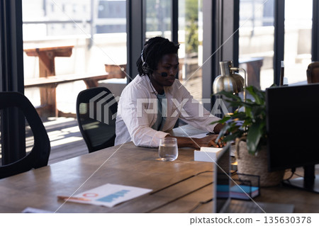Man wearing headset working on computer in modern office, focusing on tasks 135630378