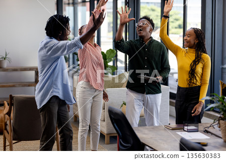 Diverse team celebrating success with high fives in modern office space 135630383